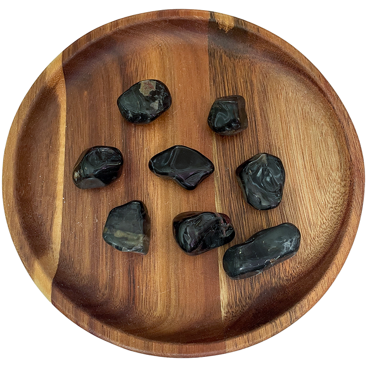 A collection of black onyx stones on a wooden plate.